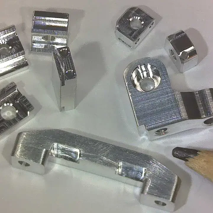 Extreem kleine aluminium onderdelen met fijnmechanische bewerkingen naast een potlood voor schaal – precisie CNC- en conventionele bewerkingen bij QNL Instrumentmakerij voor prototypes en technisch maatwerk